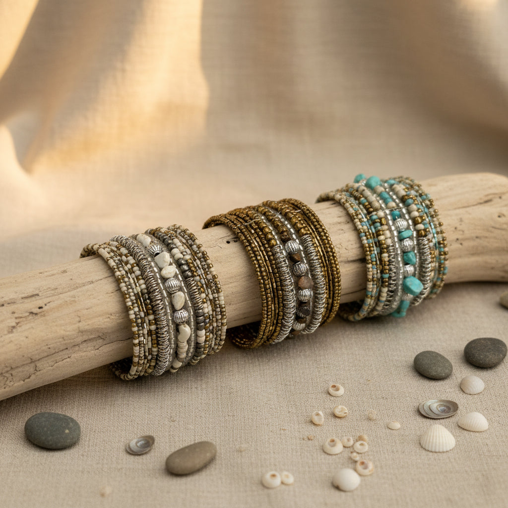 Collection of handcrafted multi-layer wrap bracelets featuring turquoise, ivory, bronze, silver, and natural stone beads, displayed on a rustic driftwood branch with decorative shells and stones on a neutral linen surface.
