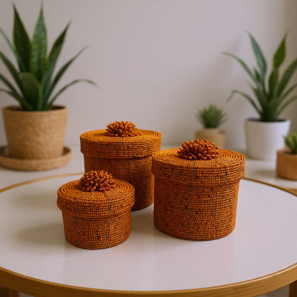 Set of three handcrafted cylindrical storage baskets with warm amber wooden beads, matching fitted lids, and decorative beaded handles, beautifully styled on a tabletop to add natural texture and elegant storage to contemporary interiors.