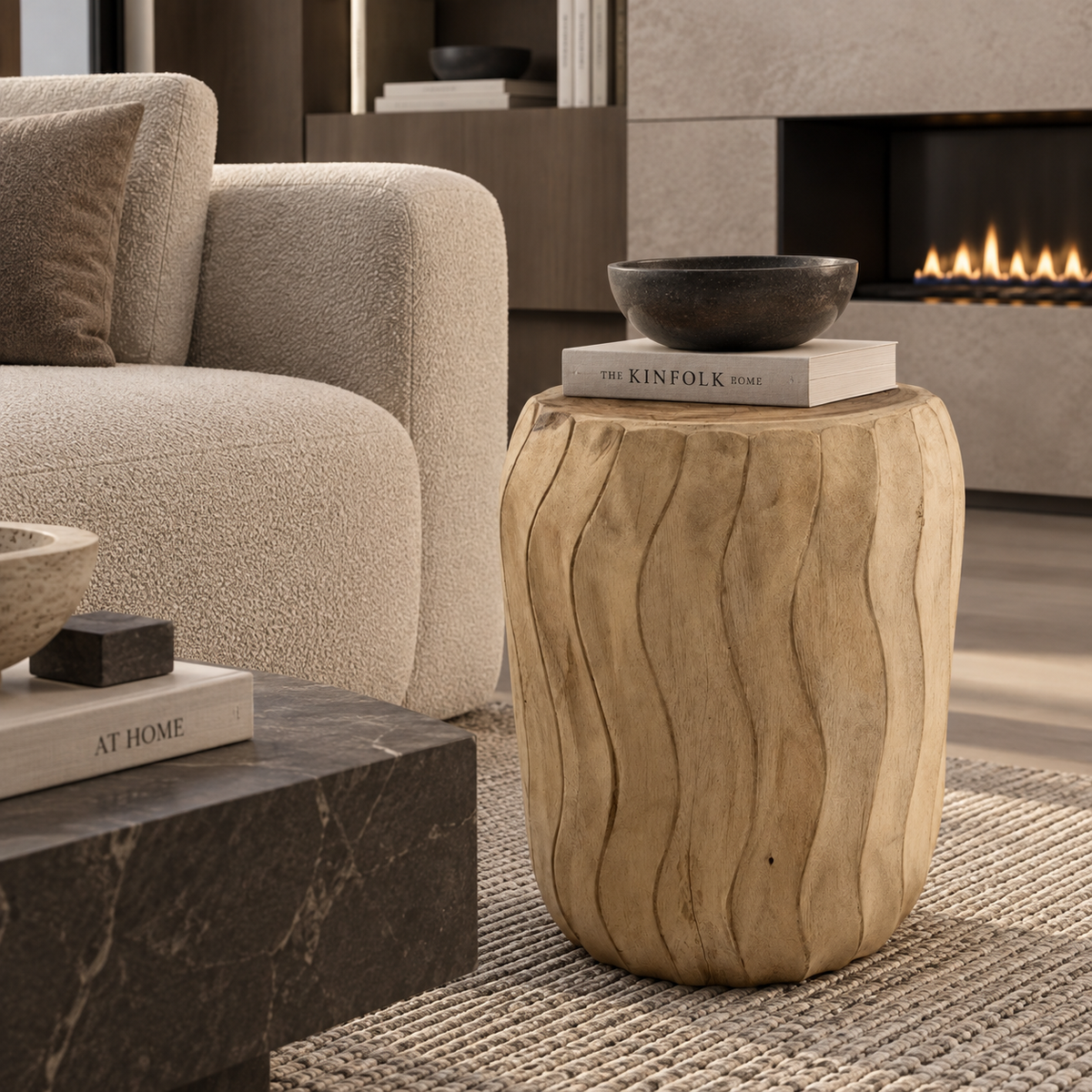 A natural wood barrel-shaped side table with wavy grain patterns, styled in a modern living room next to a beige textured sofa and a fireplace.