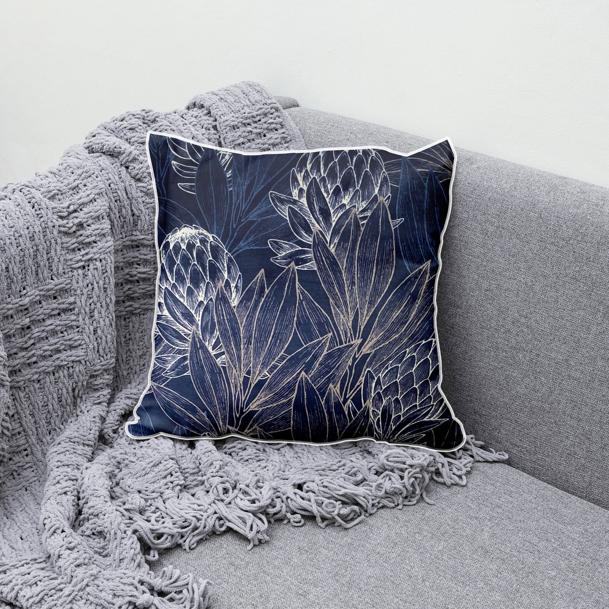 Decorative navy blue scatter cushion featuring elegant protea flowers and botanical linework in soft silver and white tones, finished with contrasting light piping.