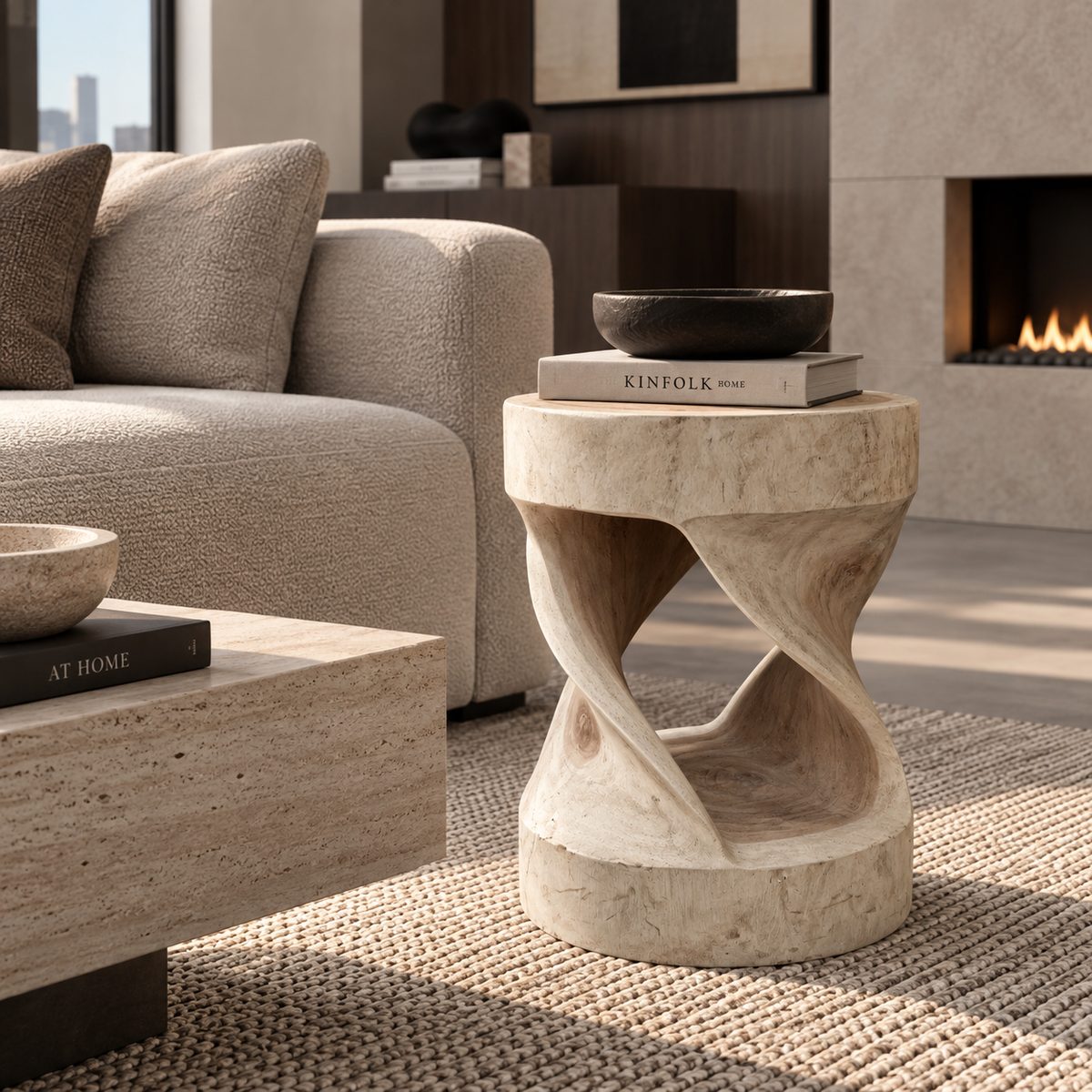 A sculptural stone side table with twisted spiral legs stands in a modern living room next to a beige sofa, holding a dark bowl and a book.