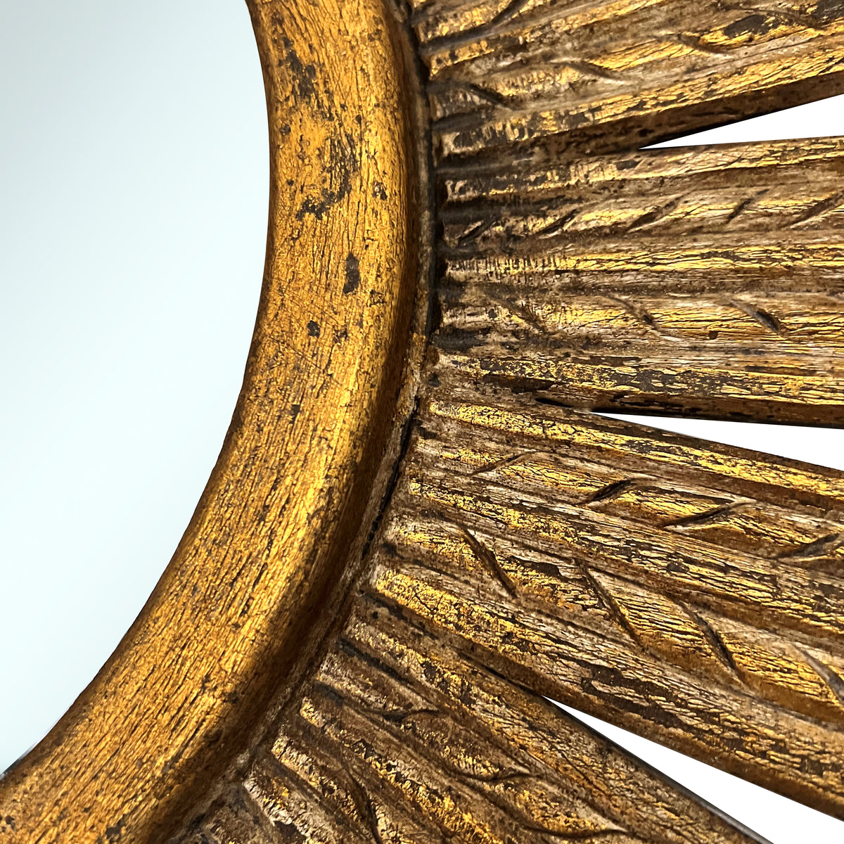 Close-up of an antique gold sunburst wall mirror featuring a textured radial frame with carved detailing and a distressed metallic finish, highlighting its handcrafted character.