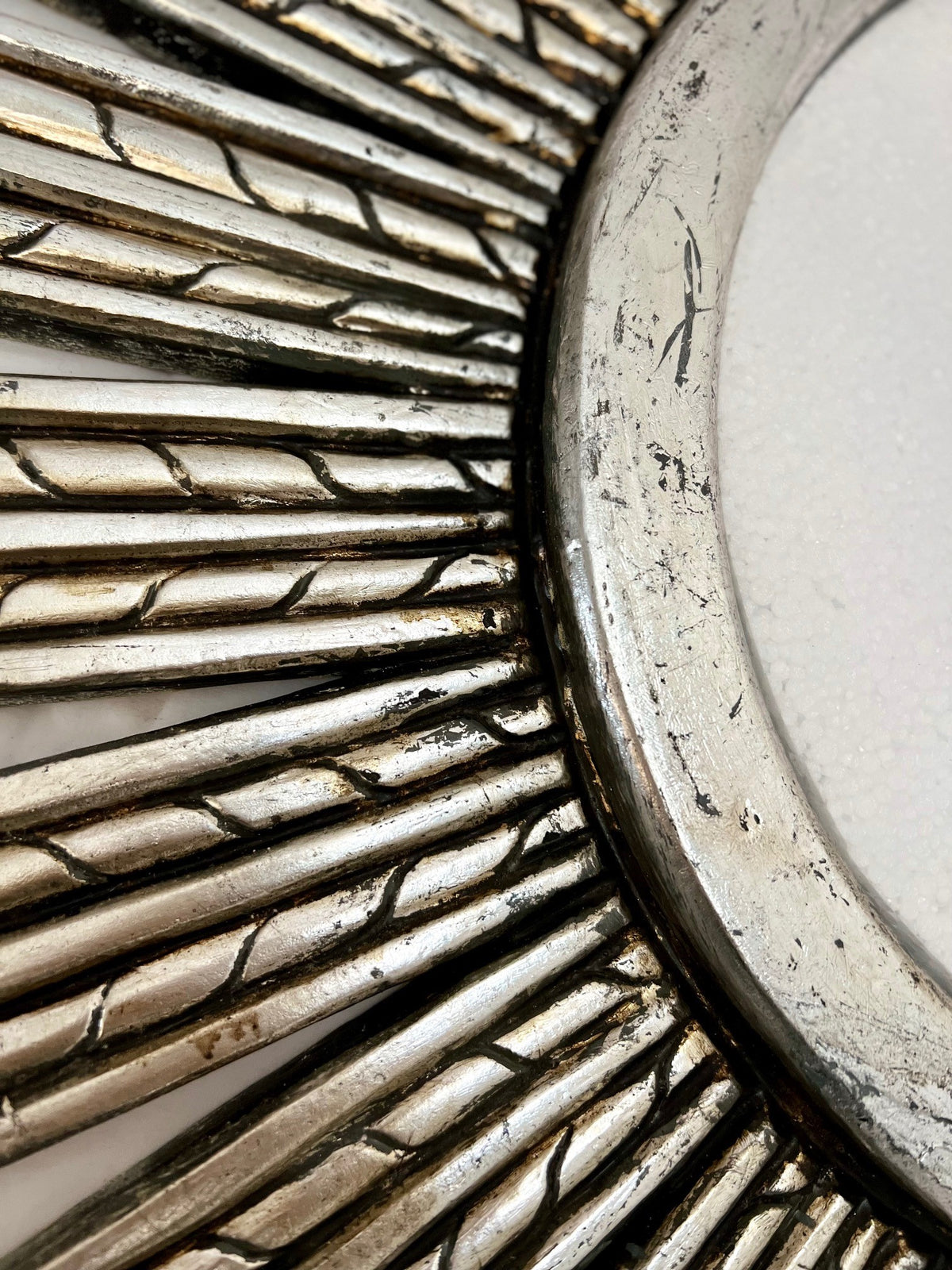 Close-up of an antique silver sunburst wall mirror featuring a textured radial frame with carved detailing and a distressed metallic finish, showcasing its handcrafted character and elegant design.