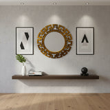 Round brushed gold geometric wall mirror with a bold Greek key-inspired frame, styled between modern framed artwork in a contemporary living room.
