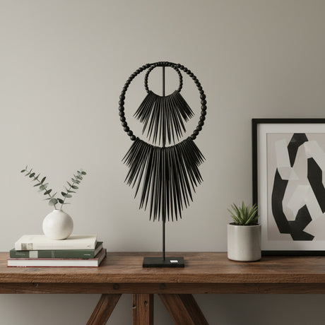 Handcrafted black beaded tribal sculpture mounted on a metal stand, featuring layered circular beadwork and dramatic fringe detailing. A contemporary African-inspired decorative accent for consoles, shelves, and tabletops in modern, minimalist, or luxury interiors.