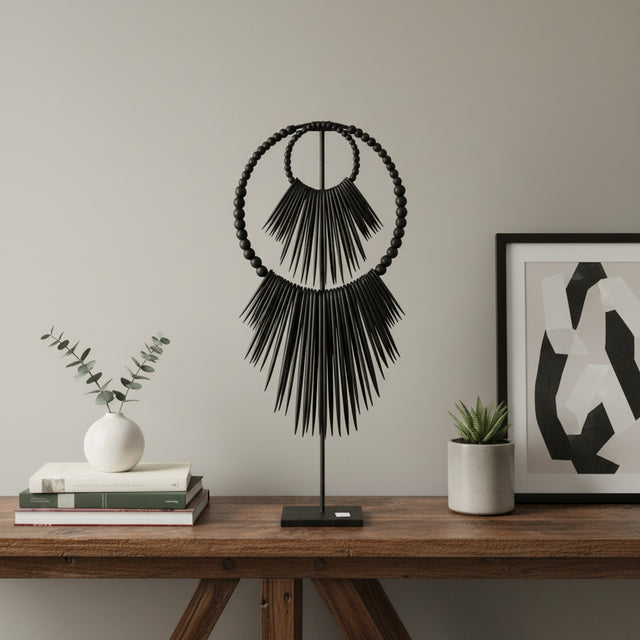 Handcrafted black beaded tribal sculpture mounted on a metal stand, featuring layered circular beadwork and dramatic fringe detailing. A contemporary African-inspired decorative accent for consoles, shelves, and tabletops in modern, minimalist, or luxury interiors.