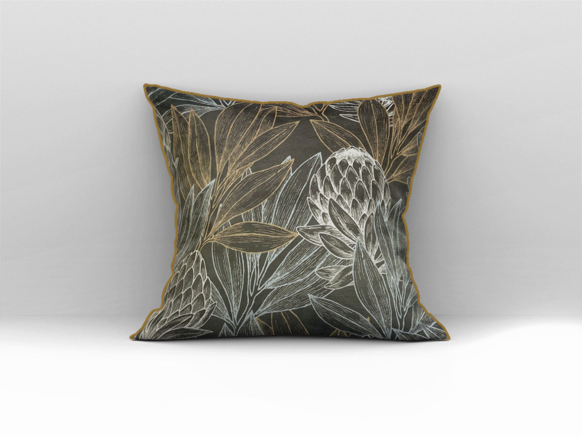 Decorative scatter cushion featuring elegant protea flowers and botanical leaves in black, charcoal, gold, and soft silver tones with coordinating gold piping.