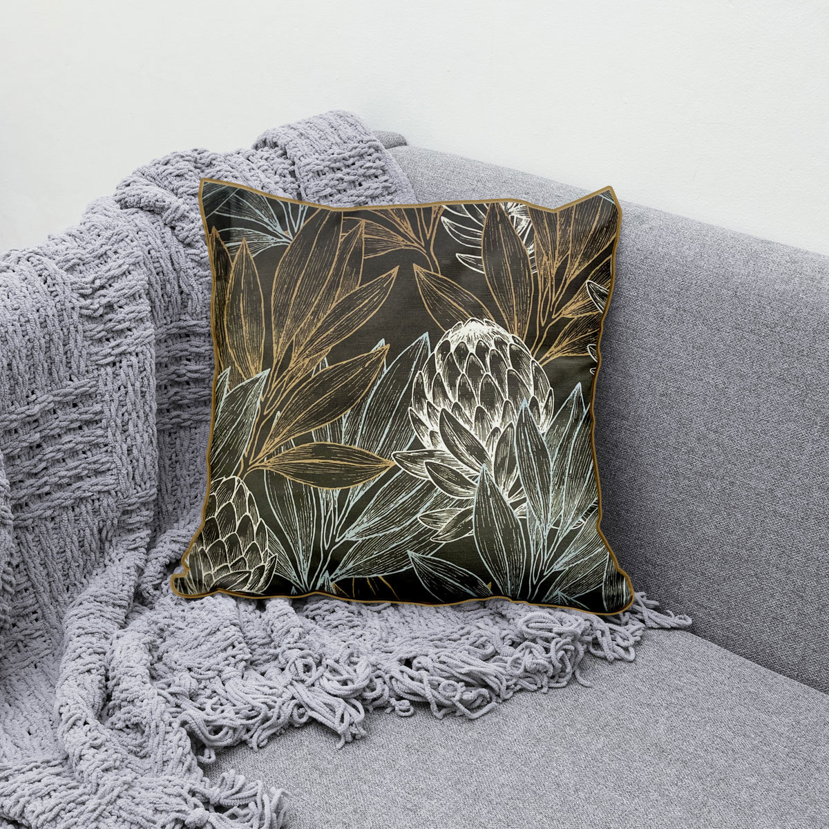 Decorative scatter cushion featuring elegant protea flowers and botanical leaves in black, charcoal, gold, and soft silver tones with coordinating gold piping.