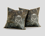 Set of three decorative scatter cushions featuring striking protea flowers and botanical leaves in black, charcoal, gold, and soft silver tones with coordinating gold piping.