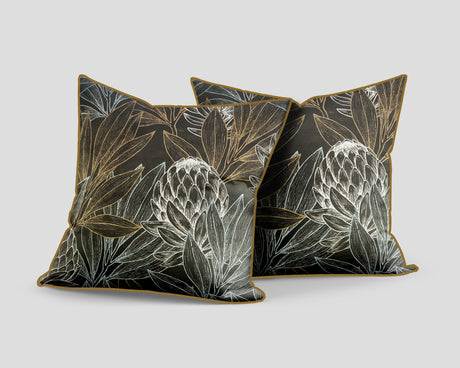 Set of three decorative scatter cushions featuring striking protea flowers and botanical leaves in black, charcoal, gold, and soft silver tones with coordinating gold piping.