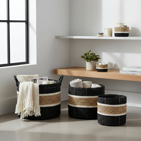 Set of three black, natural beige and cream striped woven storage baskets in varying sizes, styled with blankets and home accessories in a modern interior.