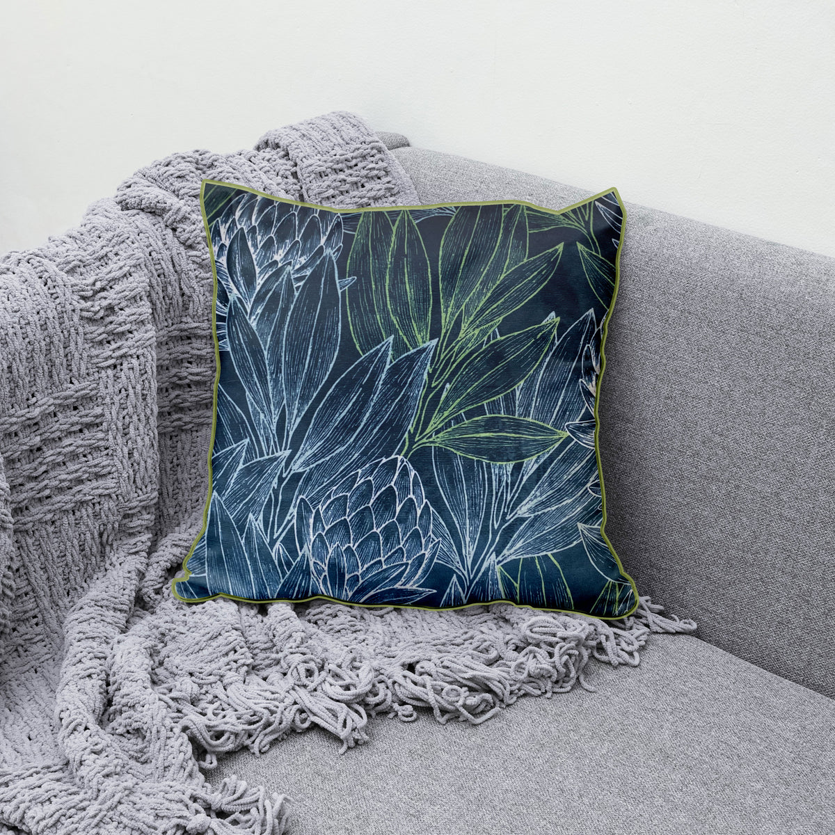 Decorative blue scatter cushion featuring an elegant protea and botanical leaf pattern with contrasting green piping, perfect for adding colour and texture to stylish interiors.