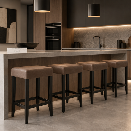 Four backless bar stools with rectangular brown upholstered seats, black tapered legs, and footrests arranged along a kitchen island.