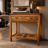 A rustic carved wooden console table with two drawers and an open lower shelf, styled in a modern living room setting with decorative objects on top.