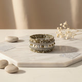 Handcrafted multi-layer wrap bracelet featuring champagne, ivory, silver, and gold-toned seed beads with pearl-inspired accents, displayed on a light stone surface against a soft neutral background.