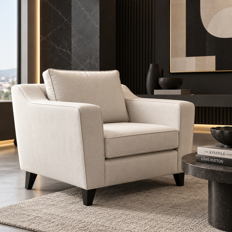 A modern beige upholstered armchair with dark tapered legs, styled in a contemporary living room setting next to a dark round coffee table.