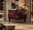 A dark reddish-brown wooden console table with curved legs and ornate metal handles, styled in a luxurious modern interior with a lamp, books, and decorative bowls on top.