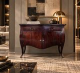 A dark reddish-brown wooden console table with curved legs and ornate metal handles, styled in a luxurious modern interior with a lamp, books, and decorative bowls on top.