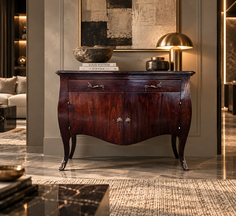 A dark reddish-brown wooden console table with curved legs and ornate metal handles, styled in a luxurious modern interior with a lamp, books, and decorative bowls on top.