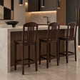 Three dark wood bar stools with tall vertical slat backrests, wooden seats, straight legs, and rectangular footrests beside a kitchen island.
