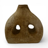 Handcrafted sculptural stoneware vase with a warm earthy finish, featuring a rounded organic silhouette, two asymmetrical cut-out openings, and a narrow neck. A contemporary decorative statement piece that adds texture, artistic character, and modern elegance to shelves, console tables, coffee tables, or styled interiors.