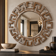 Round decorative wall mirror with a distressed brown Greek key frame, mounted on a beige wall above a console table with decorative bowls and vases.