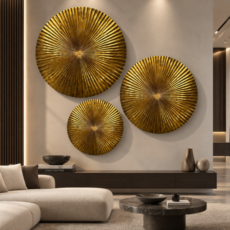 Three large round gold metallic sunburst wall art pieces mounted on a beige wall above a dark console table in a modern living room setting.