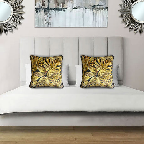 Decorative scatter cushion featuring a rich tropical botanical leaf pattern in gold, mustard, black, and earthy tones, styled on an elegant upholstered bed.