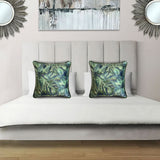 Decorative scatter cushion featuring a lush tropical botanical pattern in layered green and deep blue tones with coordinating dark piping, styled on an elegant upholstered bed.