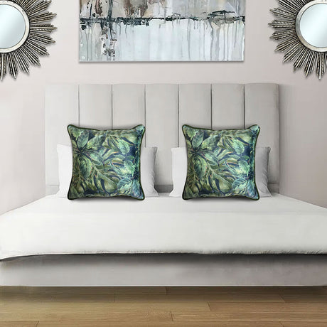 Decorative scatter cushion featuring a lush tropical botanical pattern in layered green and deep blue tones with coordinating dark piping, styled on an elegant upholstered bed.