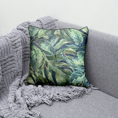 Decorative scatter cushion featuring a lush tropical leaf pattern in layered green, sage, and deep blue tones with coordinating dark green piping.