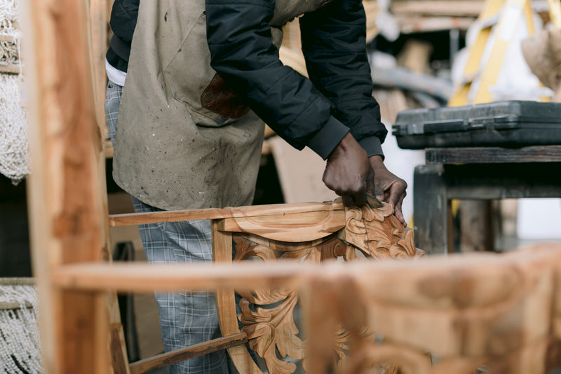 Skilled artisan hand-carving an ornate solid wood furniture frame in a woodworking workshop. Showcasing traditional craftsmanship, intricate detailing, and the bespoke furniture-making process behind luxury handcrafted pieces.