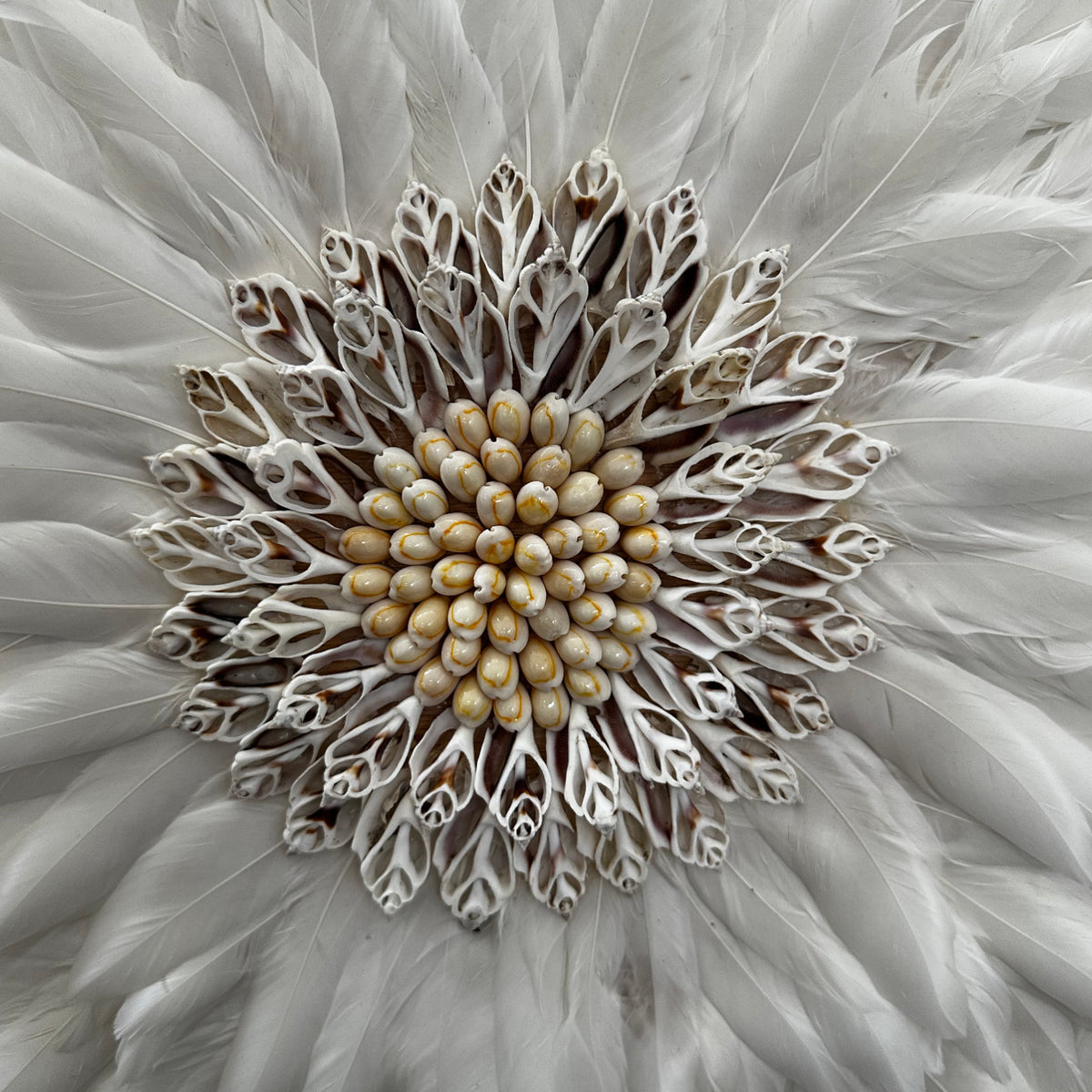 Handcrafted Juju wall décor featuring layers of soft white feathers with a decorative seashell-inspired centre, creating a luxurious statement piece with natural texture and elegance. Perfect for living rooms, bedrooms, boutique hotels, entryways, or contemporary and coastal-inspired interiors.
