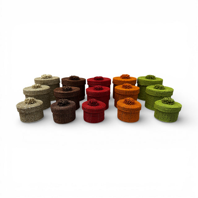 Collection of handcrafted cylindrical beaded storage baskets with matching fitted lids, available in natural, chocolate brown, ruby red, amber, and olive green finishes, perfect for stylish storage and decorative organization in any home.
