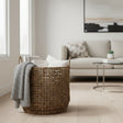 Handwoven natural fiber storage basket with integrated handles, styled with a knitted throw, decorative cushions, and books in a modern living room, offering stylish storage for blankets and home essentials.
