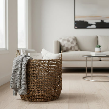 Handwoven natural fiber storage basket with integrated handles, styled with a knitted throw, decorative cushions, and books in a modern living room, offering stylish storage for blankets and home essentials.