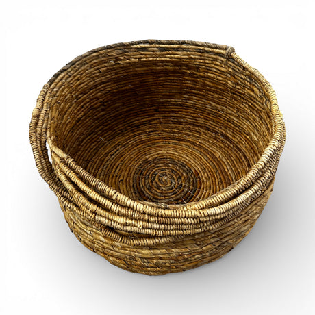 Handwoven natural storage basket with a rounded silhouette, integrated carry handles, and a tightly woven interior, ideal for storing blankets, cushions, toys, or everyday essentials while adding warm organic texture and timeless artisanal style to contemporary, coastal, or rustic interiors.