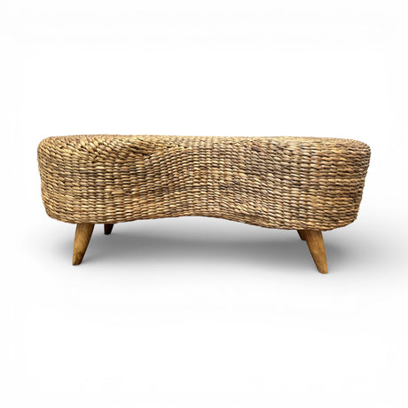 Handwoven natural rattan bench with a sculptural organic silhouette and solid wooden legs, offering a warm textured finish and stylish seating for entryways, bedrooms, living rooms, or covered outdoor spaces.