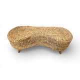 Handwoven natural rattan bench with a sculptural curved silhouette, rounded edges, and solid wooden legs, combining artisanal craftsmanship with warm organic texture for stylish seating in entryways, bedrooms, living rooms, or covered outdoor spaces.