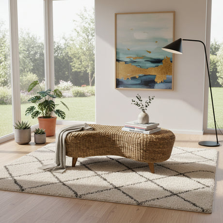 Handwoven natural rattan ottoman coffee table with a sculptural organic silhouette and wooden legs, styled with books and décor in a bright contemporary living room, adding warmth, texture, and relaxed modern elegance.
