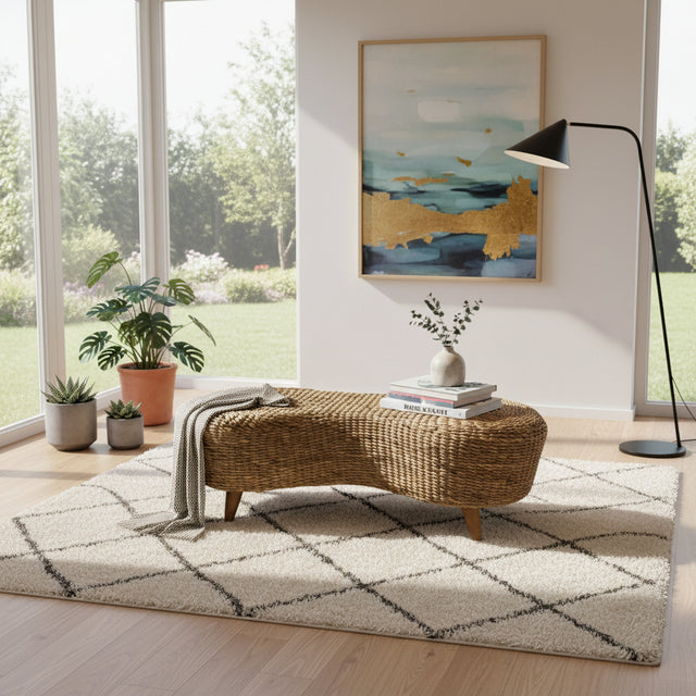 Handwoven natural rattan ottoman coffee table with a sculptural organic silhouette and wooden legs, styled with books and décor in a bright contemporary living room, adding warmth, texture, and relaxed modern elegance.