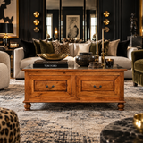 A rustic wooden coffee table with two drawers and dark metal handles, styled in a luxurious modern living room with a patterned rug, a cream sofa, and dark wood walls.