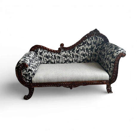 Elegant chaise lounge featuring a richly hand-carved dark wood frame, rolled arms, black and grey patterned upholstery, a plush light grey seat cushion, and a matching bolster pillow. A luxurious statement piece for classic, French-inspired, and contemporary interiors.
