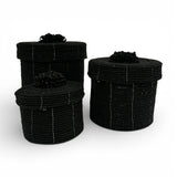 Set of three handcrafted cylindrical storage baskets with matte black wooden beads, matching fitted lids, and decorative beaded handles, perfect for stylish storage and adding a bold contemporary accent to living rooms, bedrooms, or bathrooms.