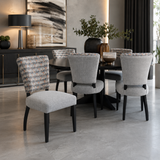 Contemporary six-seater dining set featuring a round black dining table and six upholstered dining chairs with soft grey fabric, patterned accent backrests, and black wooden legs. A stylish and elegant choice for modern dining rooms and open-plan living spaces.