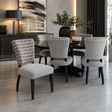 Contemporary six-seater dining set featuring a round black dining table and six upholstered dining chairs with soft grey fabric, patterned accent backrests, and black wooden legs. A stylish and elegant choice for modern dining rooms and open-plan living spaces.