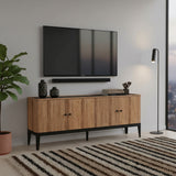 Modern oak wood TV unit with four cabinet doors, sleek black handles, and tapered black legs, styled beneath a wall-mounted television in a contemporary living room.