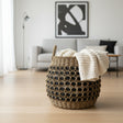 Woven basket with a white blanket on a wooden floor in a living room.