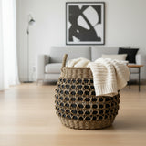 Woven basket with a white blanket on a wooden floor in a living room.
