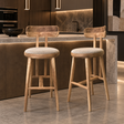 Two natural wood bar stools with curved backrests, round cream upholstered seats, tapered legs, and wooden footrests.